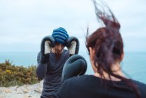 Man and woman in boxing gloves punching each other while standing on sea coast — Stock Photo