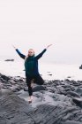 Giovane donna con le mani alzate meditare e in piedi su rocce vicino alla costa del mare — Foto stock