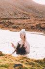Молодая женщина в шляпе и купальнике с закрытыми глазами медитирует на поверхности воды у скалистого берега — стоковое фото