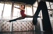 Giovane ballerina sottile che salta fuori terra in studio flettendo le gambe. — Foto stock