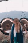 Young blond woman with mallets near ritual gongs between lands and hills — Stock Photo