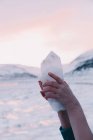 Mani di donna che tiene roccia di cristallo vicino alle montagne e cielo rosa su sfondo sfocato — Foto stock