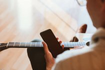 Рука человека, играющего на гитаре с мобильным телефоном — стоковое фото