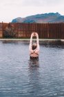 Visão traseira da jovem que descansa na água da piscina contra cerca de madeira na natureza com montanha no fundo — Fotografia de Stock