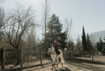 Douce petite fille en casque chevauchant obéissant cheval blanc dans l'enceinte pendant la leçon le jour de l'automne sur ranch — Photo de stock