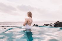 Giovane donna che medita in acqua di piscina vicino a rocce e cielo nuvoloso — Foto stock
