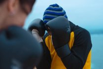 Крупним планом чоловік і жінка в боксерських рукавичках гладять один одного, стоячи на морському узбережжі — стокове фото