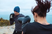 Чоловік і жінка в боксерських рукавичках гладять один одного, стоячи на морському узбережжі — стокове фото