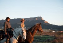 Homem e mulher montando cavalos contra o pôr do sol céu no rancho — Fotografia de Stock