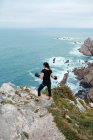 Vue arrière de la femme en gants de boxe debout sur une falaise pierreuse et regardant la mer pendant l'entraînement en plein air — Photo de stock