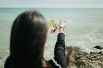 Mãos de mulher jogando pequenas flores amarelas na água do mar no dia ensolarado — Fotografia de Stock