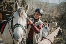 Старший чоловік в шоломі кладе мотузку на білого коня під час уроку верхової їзди на осінній день на ранчо — стокове фото