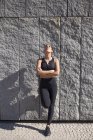 Brünette Frau in Sportkleidung steht gegen Granitwand und schaut auf — Stockfoto