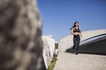 Junge brünette schlanke Frau in Sportbekleidung joggt bei sonnigem Wetter im Park — Stockfoto