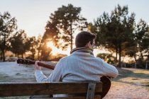 Чоловік сидить на лавці в природі і грає на гітарі — стокове фото