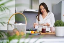 Young happy woman making sandwich at table in kitchen at home — Stock Photo