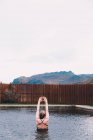 Vue arrière de la jeune femme reposant dans l'eau de la piscine contre une clôture en bois dans la nature avec montagne sur fond — Photo de stock
