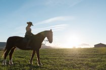 Woman riding horse against sunset sky on ranch — Stock Photo