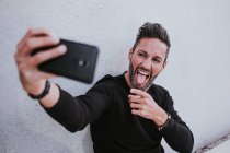 Medioevo bello elegante felice maschio in abbigliamento casual prendendo selfie sul telefono cellulare e seduto vicino al muro grigio — Foto stock