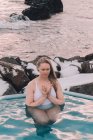 Молодая женщина с закрытыми глазами медитирует в воде бассейна возле скал — стоковое фото