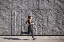 Brunette woman running on sunny morning with granite wall on background — Stock Photo