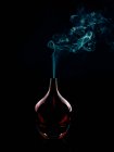 Glass bottle emitting smoke on black background — Stock Photo