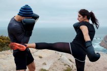 Чоловік і жінка в боксерських рукавичках вдарили один одного, стоячи на скелі проти моря і неба — стокове фото