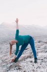 Blonde Frau beugt sich mit erhobener Hand in verschneiter Natur mit Bergen im Hintergrund — Stockfoto