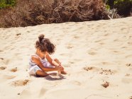 Linda niña jugando con arena en la playa - foto de stock