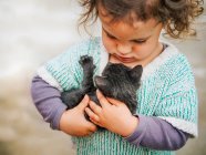 Tendre scène de mignonne petite fille tenant et berçant un petit chat noir — Photo de stock