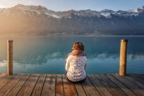 Назад вид жінка, сидячи на дереві Пірс над бірюзовим озером в снігових горах Швейцарії — стокове фото