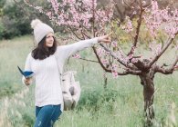 Viajante feminino com mochila e guia livreto apontando com o dedo perto da árvore florescente no campo da primavera — Fotografia de Stock