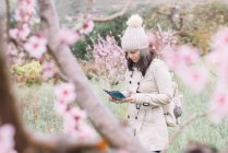 Жінка-мандрівник з рюкзаком читає путівник буклетом під час прогулянки біля квітучих дерев у весняній сільській місцевості — стокове фото
