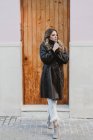 Стильна жінка в старовинному шкіряному пальто, що стоїть біля дерев'яних дверей на вулиці — стокове фото