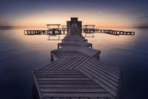 Muelle geométrico de madera vacío sobre agua tranquila sobre fondo de puesta del sol brillante - foto de stock