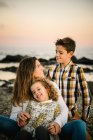 Donna di mezza età con i suoi figli sulla riva del mare sorridenti e che si abbracciano — Foto stock