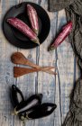 Свіжі стиглі баклажани біля шматка смугастої тканини на обвітреній дерев'яній стільниці — стокове фото