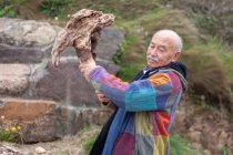 У віці чоловік в куртці ламає грубий кам'яний шматок, що стоїть на узбережжі — стокове фото