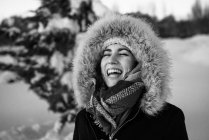 Jovem fêmea atraente em roupas quentes com pele alegre rindo ao lado coberto de neve conífera árvore — Fotografia de Stock