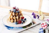 Тарелка со стопкой золотых вафель, украшенных свежими ягодами и шоколадной начинкой на столе — стоковое фото