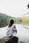 Жінка сидить на скелі біля озера і гір — стокове фото