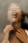 Mulher preta sensual com olhos fechados gemendo e respirando pesadamente enquanto faz sexo atrás da janela molhada — Fotografia de Stock