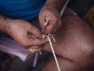 Primeros planos de artesano anónimo tejiendo hojas de palma secas de fibra mientras trabaja en taller - foto de stock
