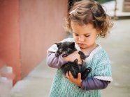 Zarte Szene eines süßen kleinen Mädchens, das eine kleine schwarze Pussycat hält und schaukelt — Stockfoto