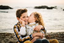 Веселые и симпатичные мальчик и девочка улыбаются и обнимают друг друга на пляже — стоковое фото