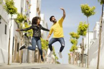 Красивый бородатый мужчина и красивая женщина кричат и прыгают вверх, делая селфи в солнечный день на городской улице — стоковое фото