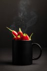 Steamy black ceramic mug full of hot chili peppers placed against dark background — Stock Photo
