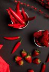 Tela roja y ramitas con brotes brillantes colocadas sobre fondo negro cerca de chiles picantes y fresas maduras dulces - foto de stock