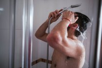 Мужчина без рубашки, не узнаваемый, принимает душ в ванной — стоковое фото