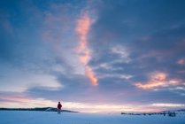 Турист в теплой одежде, стоящий на величественном снежном поле на фоне яркого закатного неба — стоковое фото